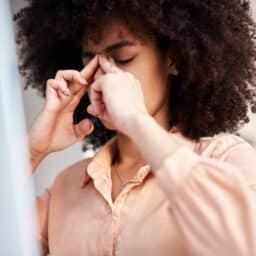 Shot of a young woman suffering with a blocked nose and headache at work