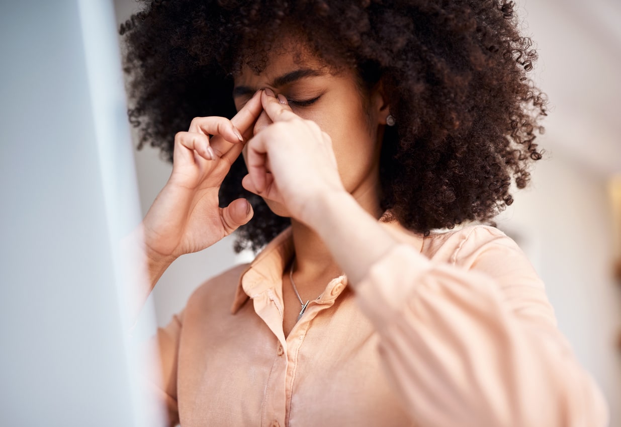 Shot of a young woman suffering with a blocked nose and headache at work.