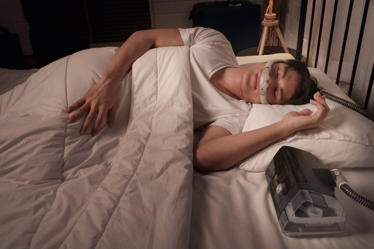 Man using CPAP mask and machine for sleep apnea treatment at home.