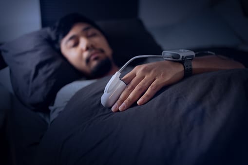 Man in bed at home with sleep monitors on his finger and sleep.