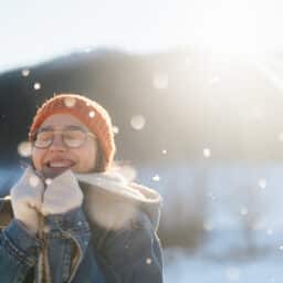 Girl smiling outside while it's snowing, the sun behind her.