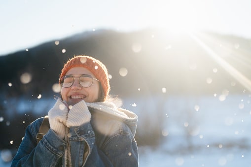 Girl smiling outside while it's snowing, the sun behind her.