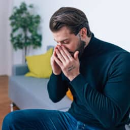 Man sitting on a couch and rubbing his sinuses.