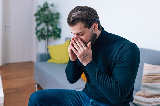 Man sitting on a couch and rubbing his sinuses.